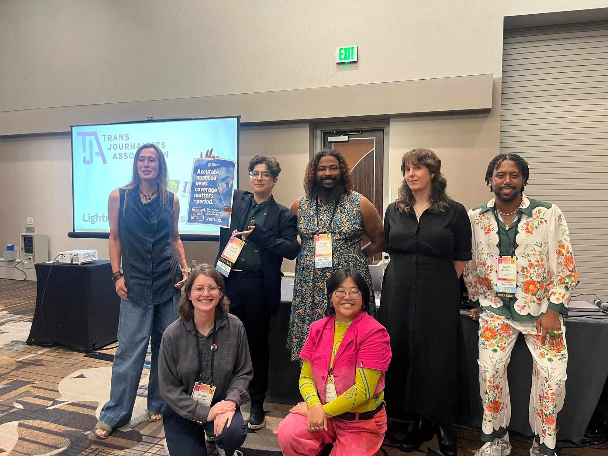 Seven journalists pose in a conference room in front of Trans Journalists Association logos